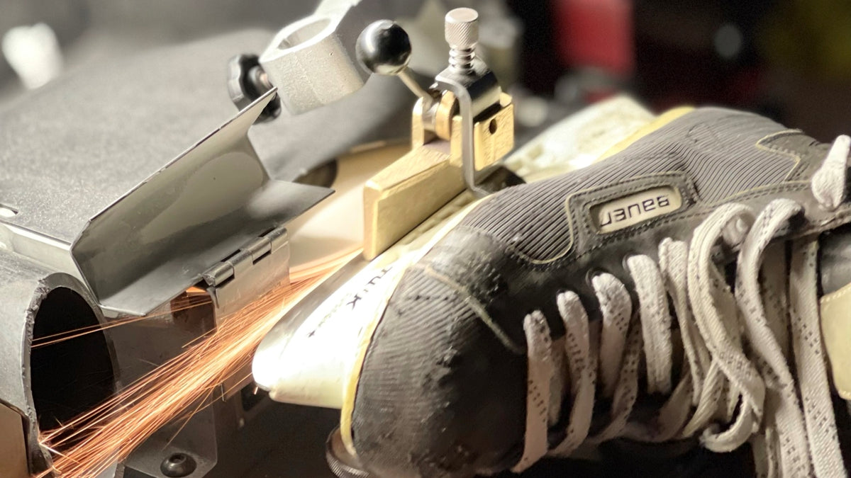 Hands guiding a hockey skate across the sharpening wheel at The Sharpening Dude